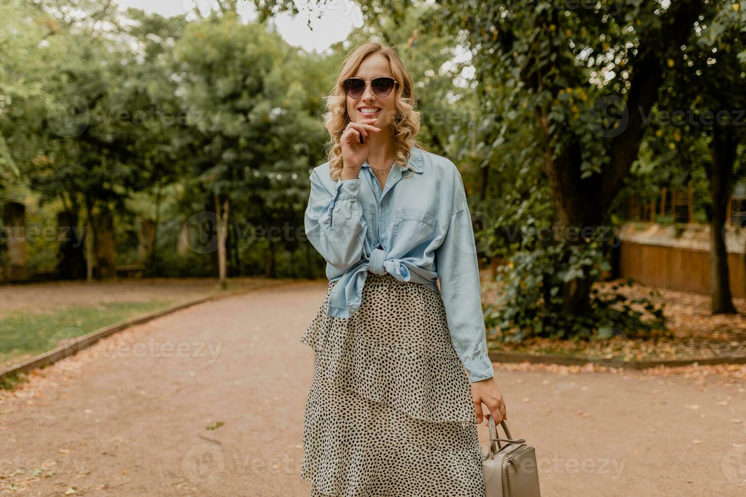 attractive blond smiling woman walking in park in stylish outfit photo