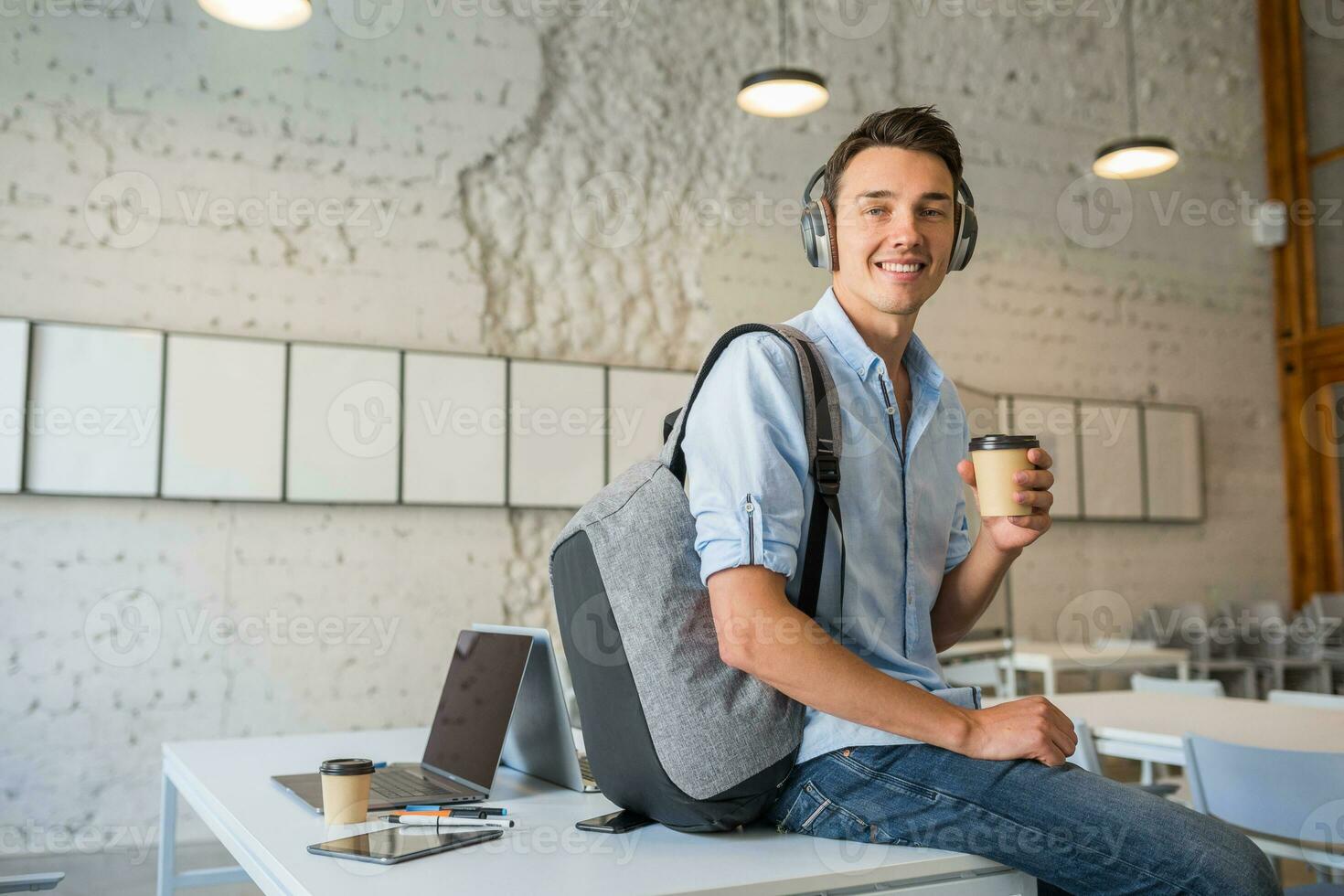 frio joven hermoso hombre sentado en mesa en auriculares con mochila en  trabajo colaborativo oficina 29049663 Foto de stock en Vecteezy