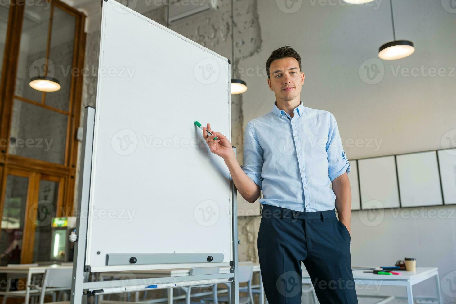 young handsome smiling man standing at empty white board with marker photo