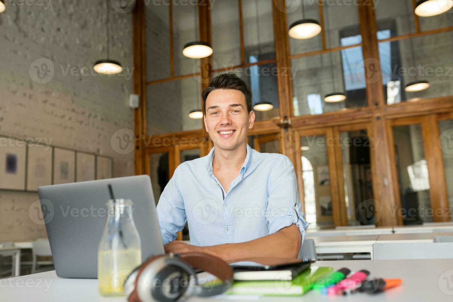 happy young confident man working on laptop, sitting in co-working office photo