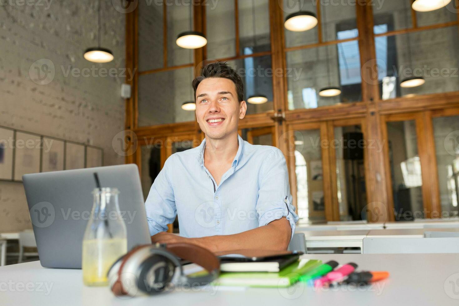 happy young confident man working on laptop, sitting in co-working office photo