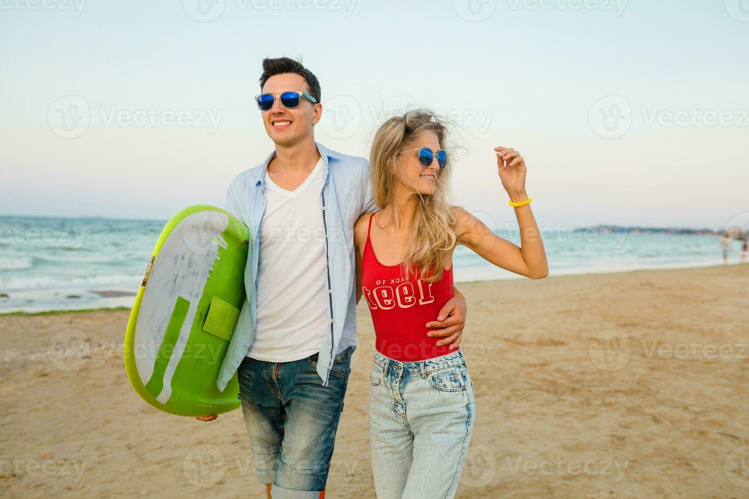 young smiling couple having fun on beach walking with surf board photo