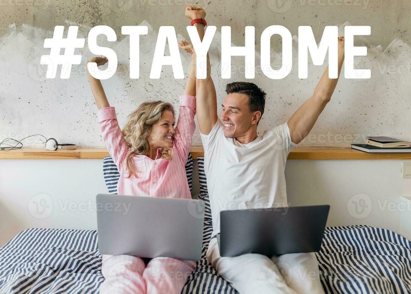 young attractive couple sitting on bed in morning in pajamas working on laptop photo