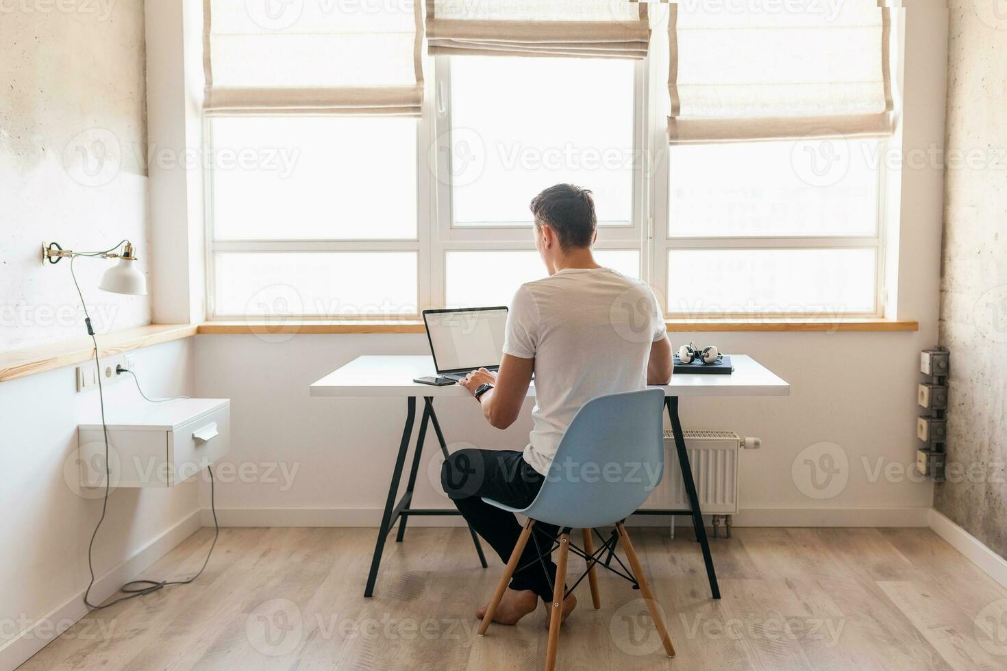 young handsome man in casual outfit sitting at table working on laptop, typing, freelancer at home photo