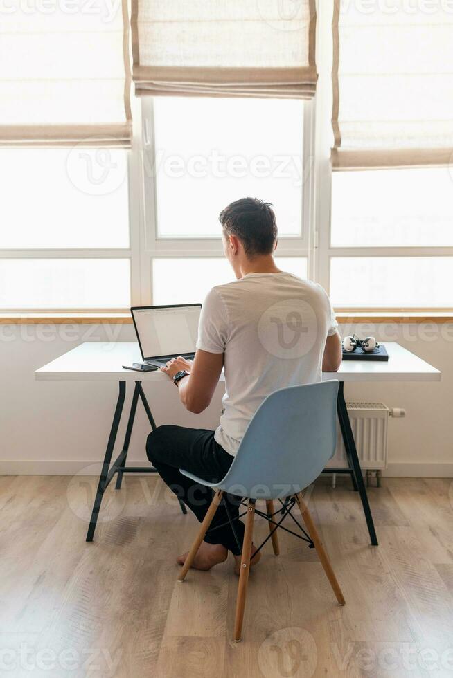 young handsome smiling man in casual outfit sitting at table working on laptop photo