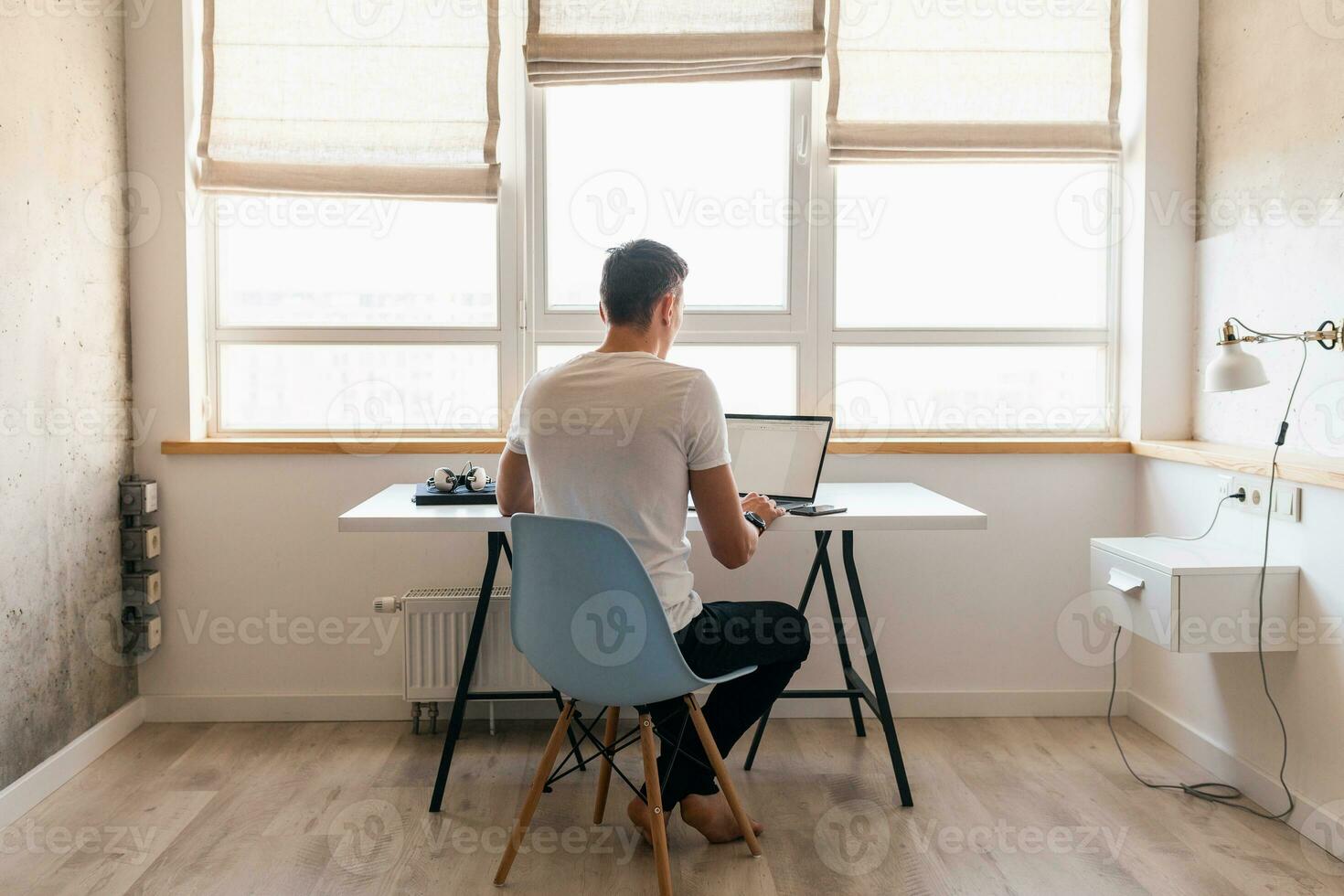 joven hermoso sonriente hombre en casual atuendo sentado a mesa trabajando en ordenador portátil foto