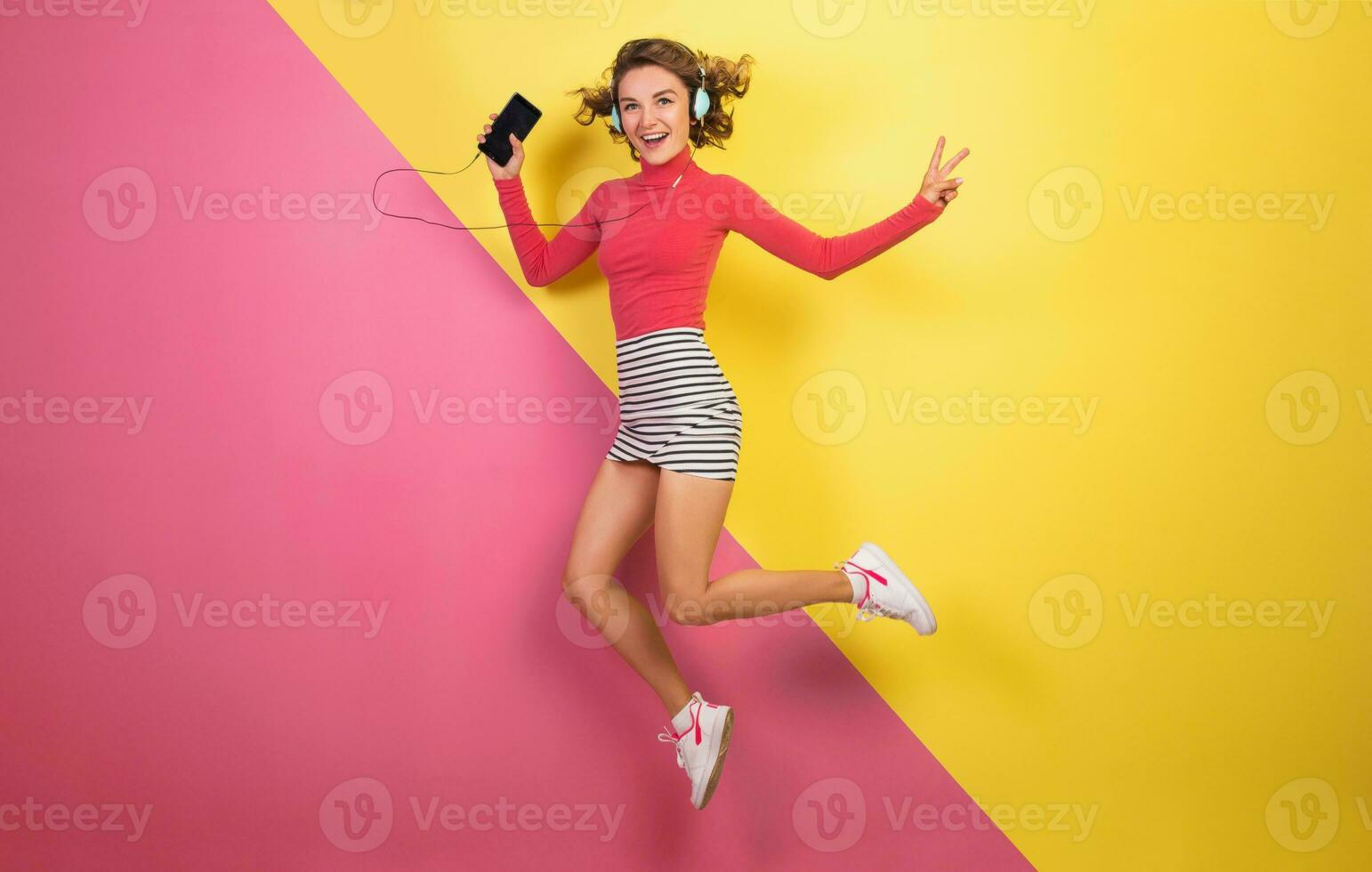 smiling attractive smiling excited woman in stylish colorful outfit jumping and listening to music photo