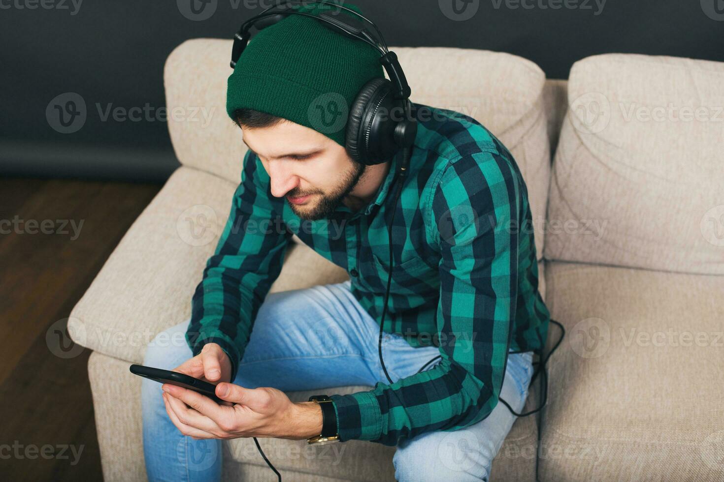 young hipster handsome bearded man sitting on a couch at home, listening to music photo