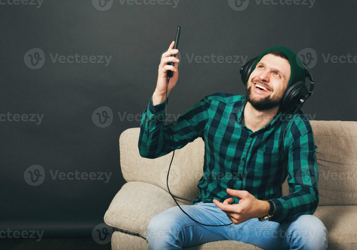 young hipster handsome bearded man sitting on a couch at home, listening to music photo