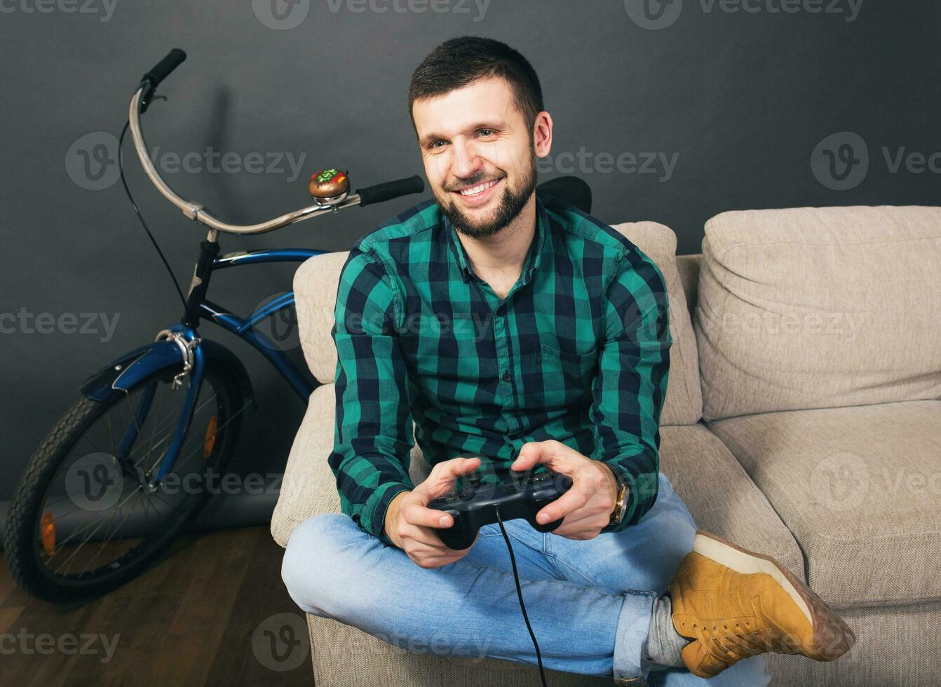 young hipster handsome bearded man sitting on couch at home, playing video game photo