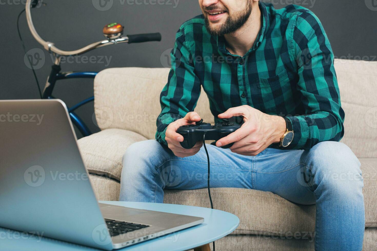 young hipster handsome bearded man sitting on couch at home, playing video game photo