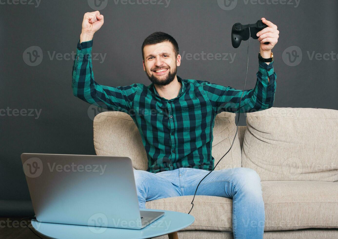 young hipster handsome bearded man sitting on couch at home, playing video game photo