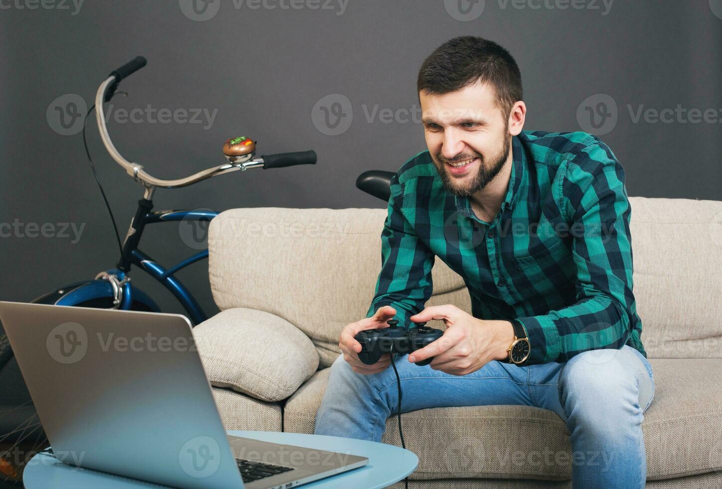 young hipster handsome bearded man sitting on couch at home, playing video game photo