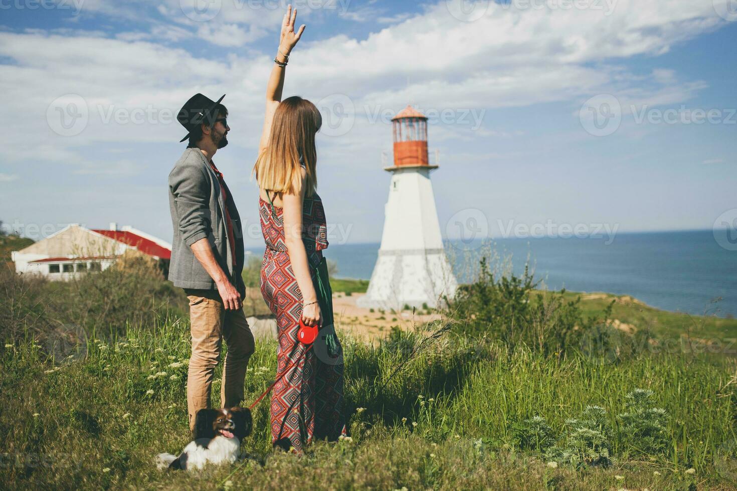 view from back on young stylish hipster couple in love walking with dog in countryside photo