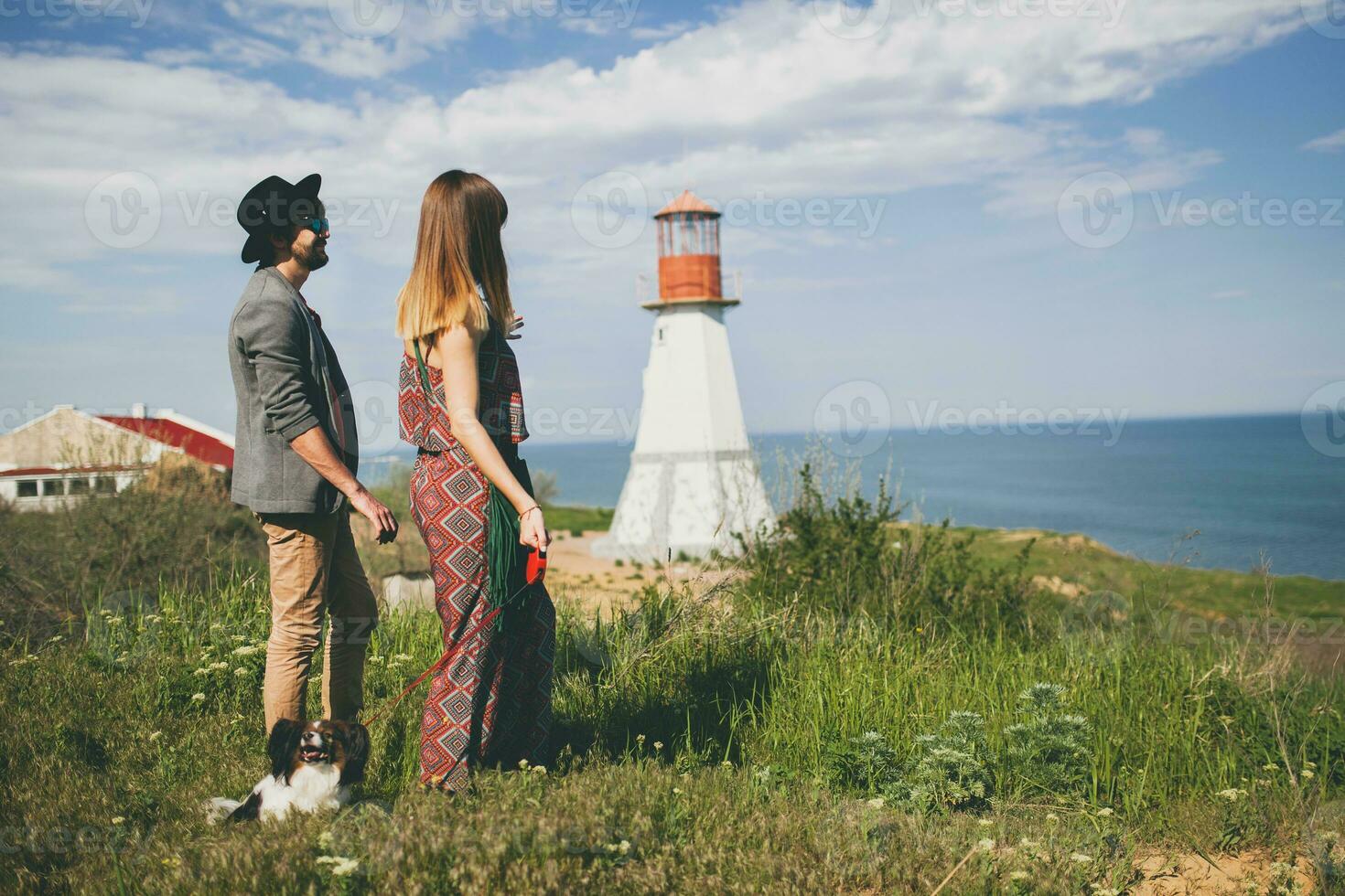 view from back on young stylish hipster couple in love walking with dog in countryside photo