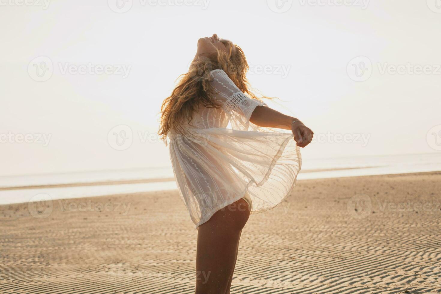 slim beautiful woman in white cotton dress walking on tropical beach photo