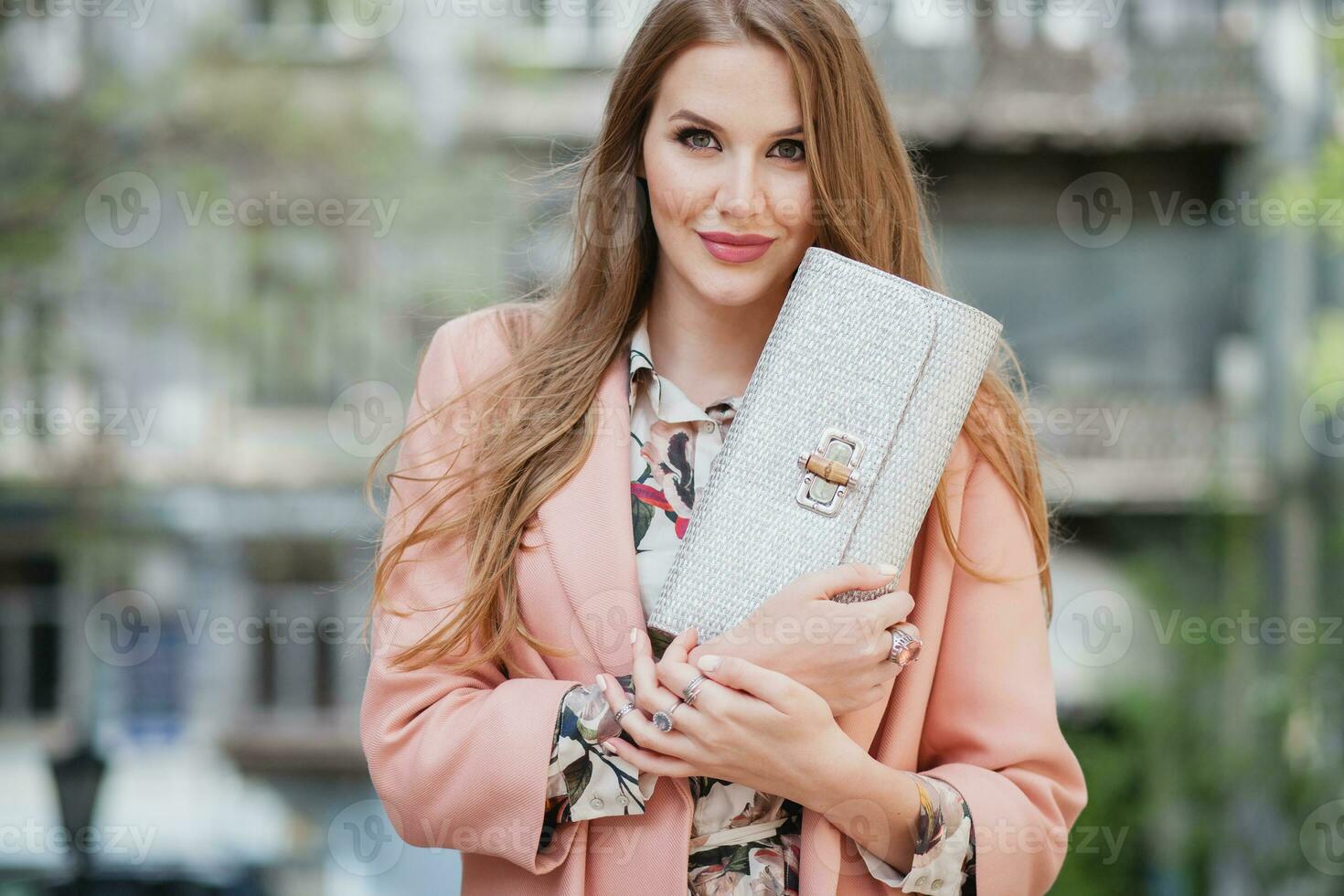 portrait of attractive stylish smiling woman walking city street in pink coat photo