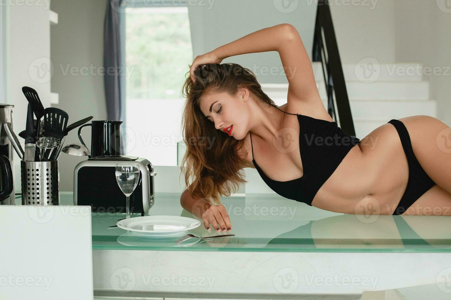 young slim beautiful woman lying on kitchen table sexy, black underwear, housewife, sensual, dinning room, household appliances, skinny body, tanned skin photo