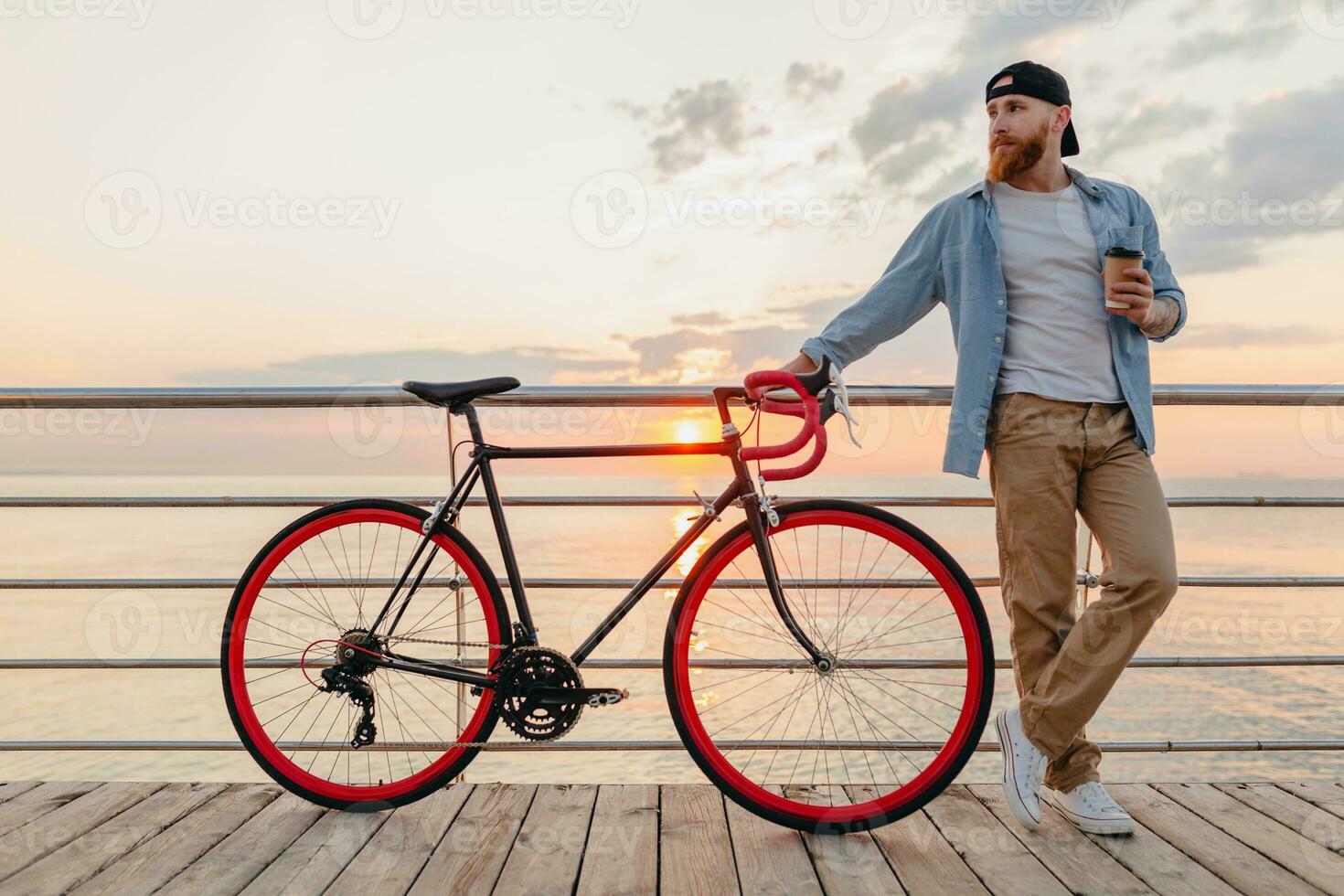 young bearded man traveling on bicycle at sunset sea photo