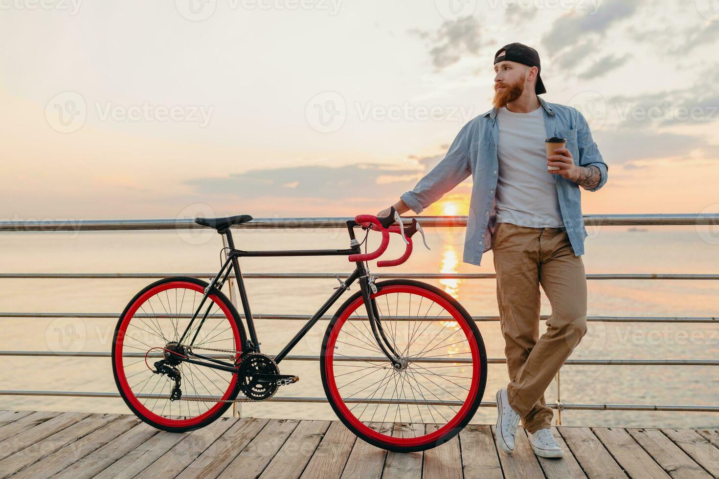 young bearded man traveling on bicycle at sunset sea photo