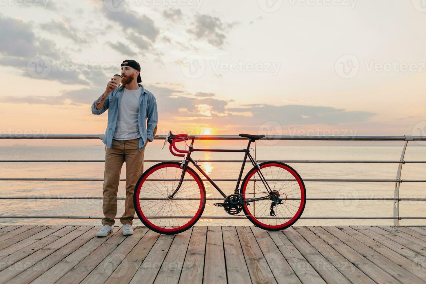 handsome bearded man traveling with bicycle in morning sunrise by the sea photo