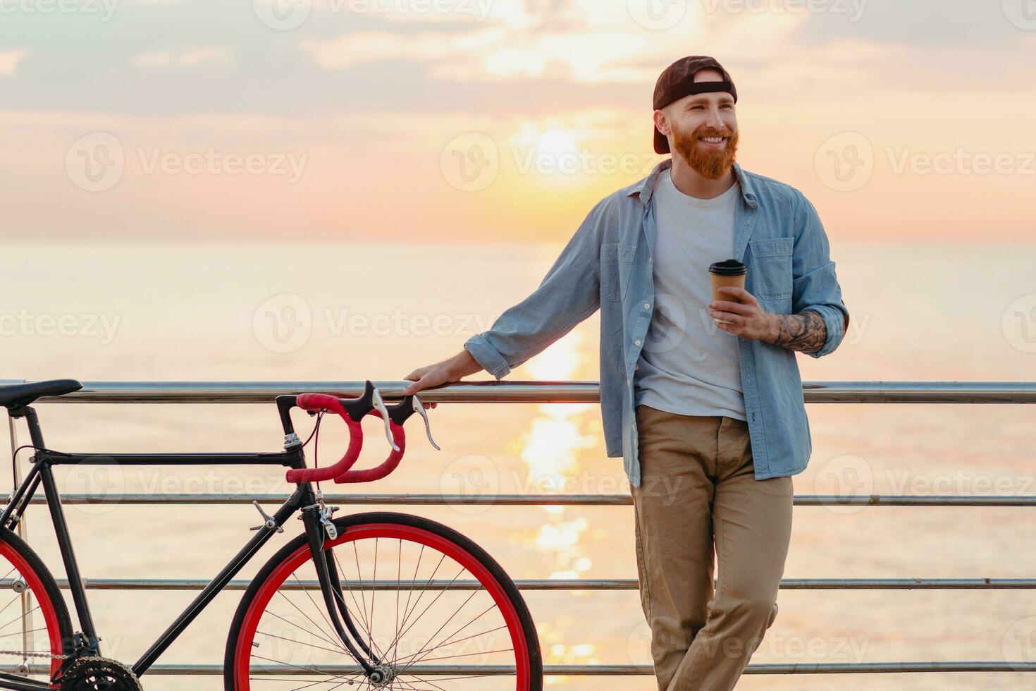 handsome bearded man traveling with bicycle in morning sunrise by the sea photo