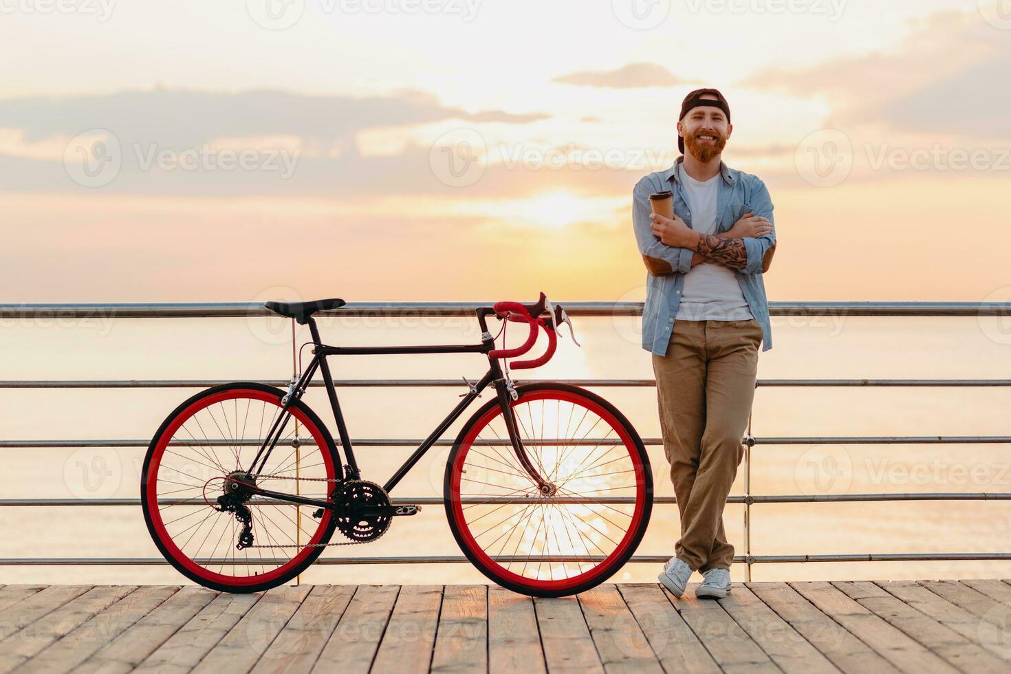 handsome bearded man traveling with bicycle in morning sunrise by the sea photo