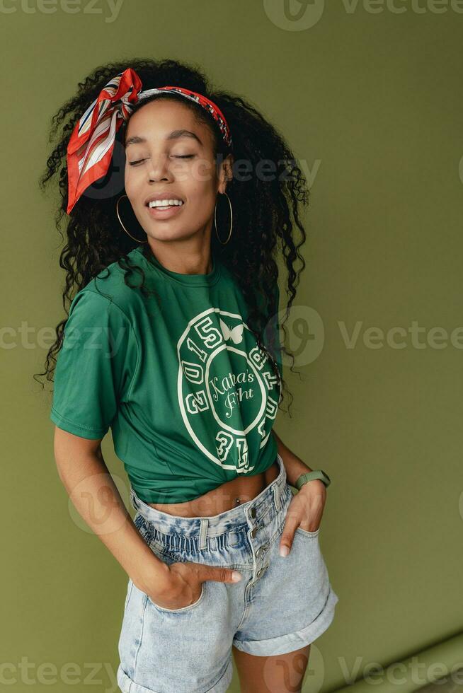 attractive black african american woman posing in stylish hipster outfit on green background photo