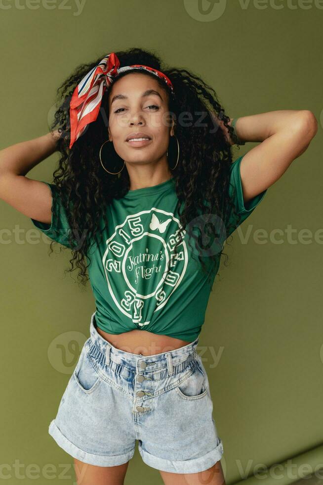 attractive black african american woman posing in stylish hipster outfit on green background photo