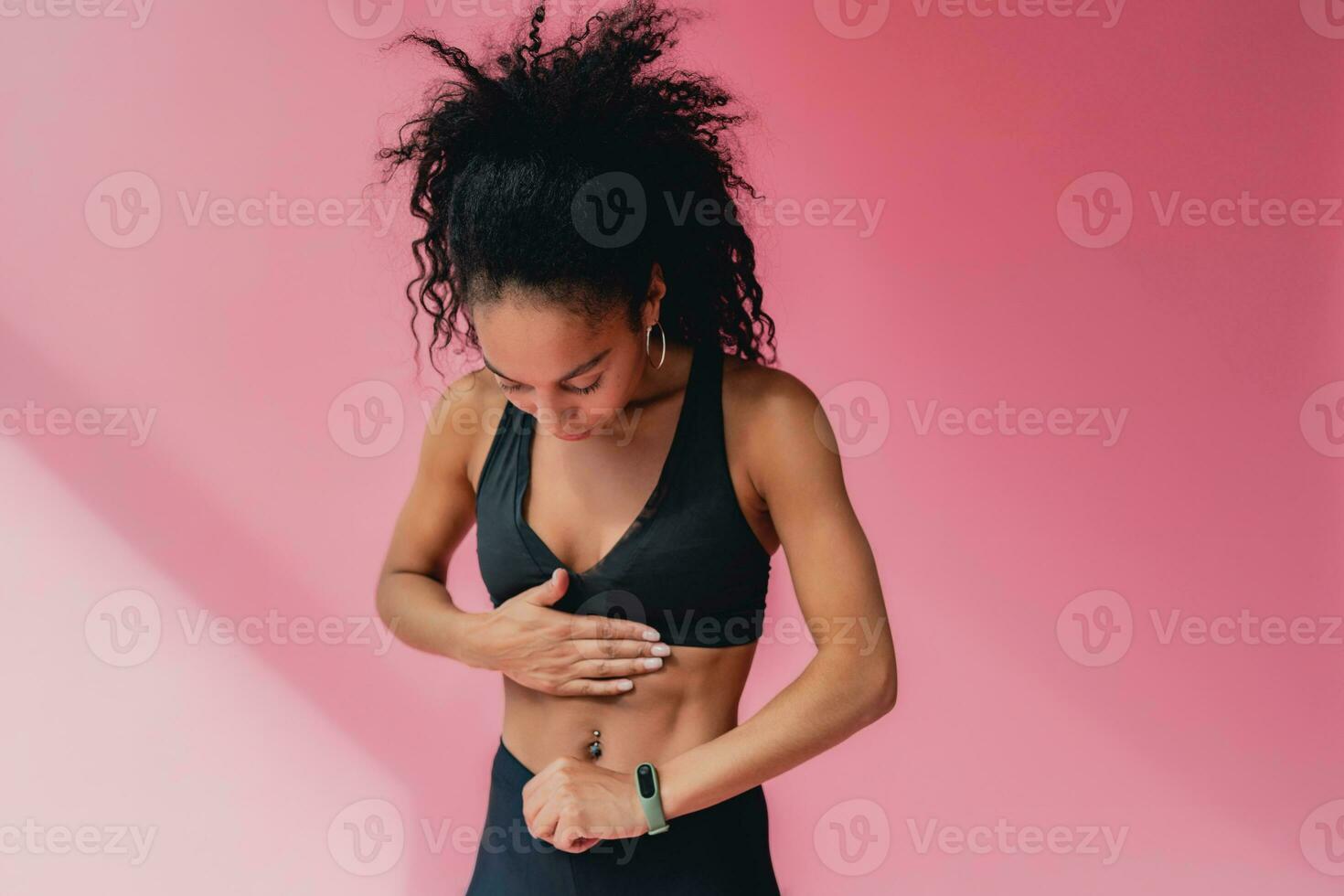 attractive black african american woman in black leggins fitness outfit on pink background photo