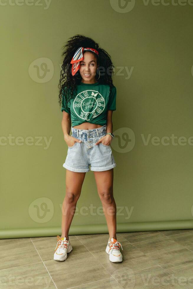 attractive black african american woman posing in stylish hipster outfit on green background photo
