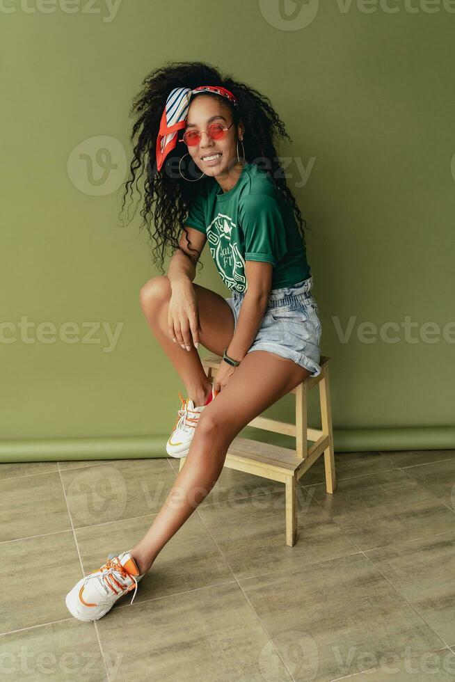 attractive black african american woman posing in stylish hipster outfit on green background photo