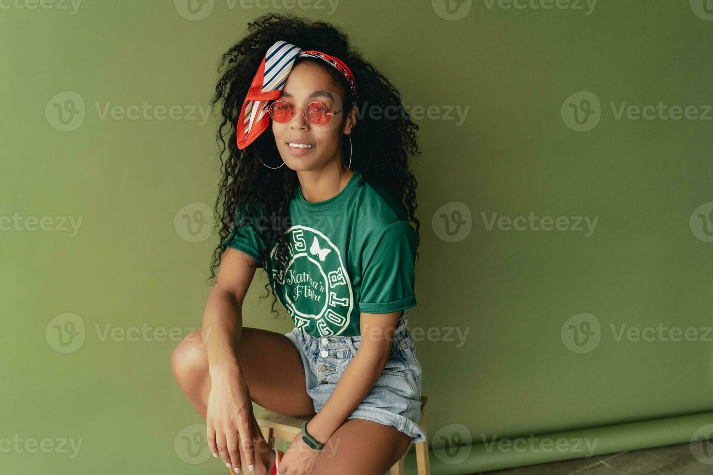 attractive black african american woman posing in stylish hipster outfit on green background photo