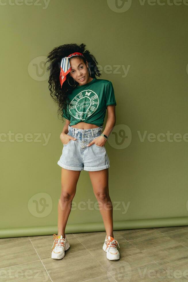 attractive black african american woman posing in stylish hipster outfit on green background photo