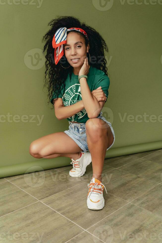 attractive black african american woman posing in stylish hipster outfit on green background photo