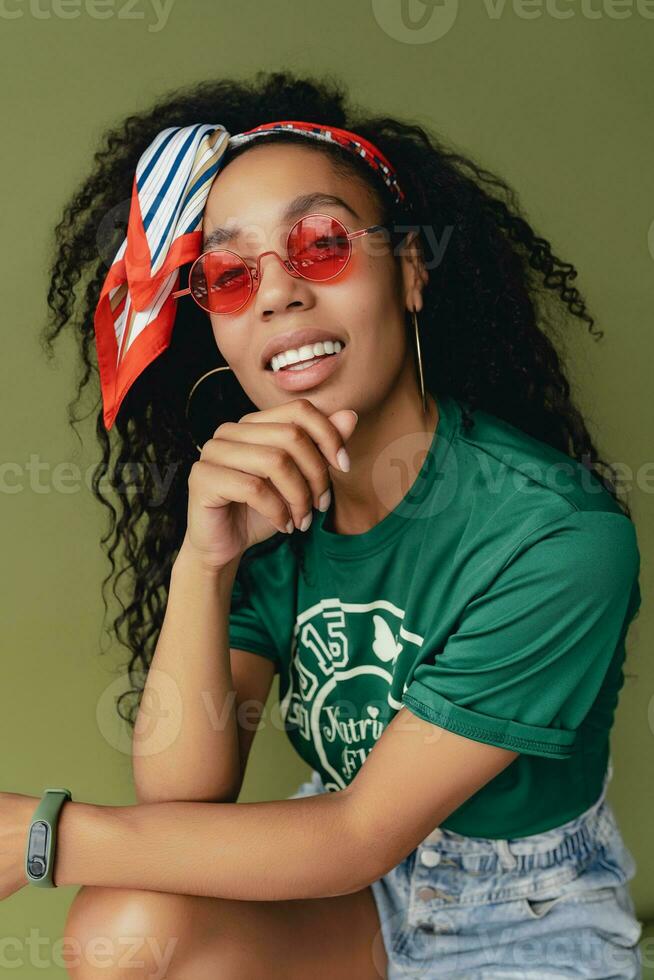 attractive black african american woman posing in stylish hipster outfit on green background photo