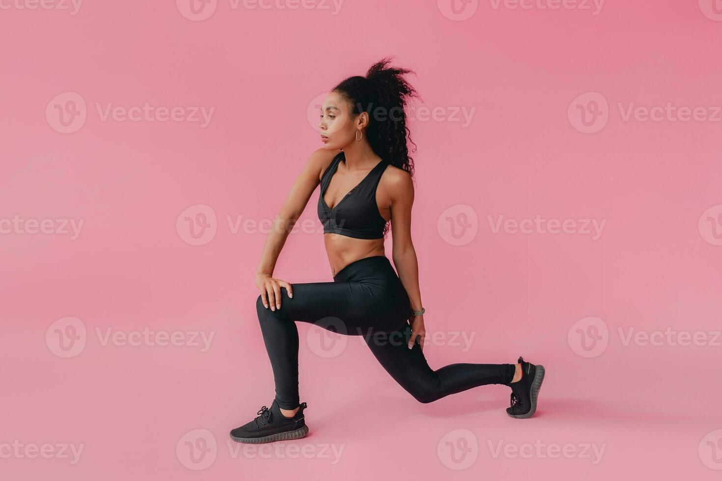 attractive black african american woman in black leggins fitness outfit on pink background photo