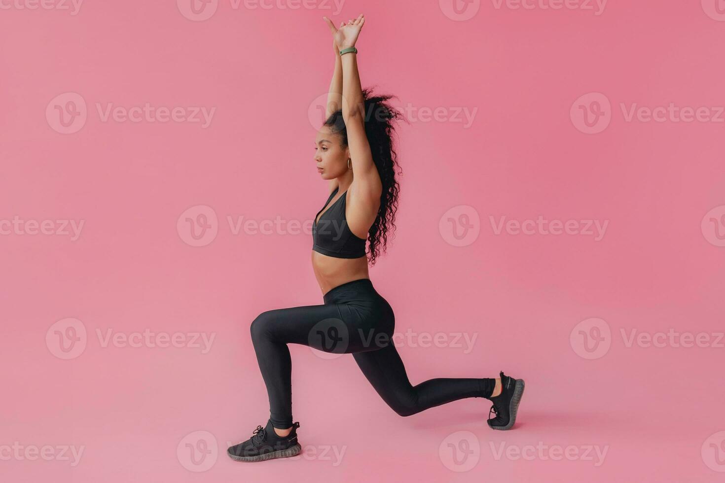 attractive black african american woman in black leggins fitness outfit on pink background photo
