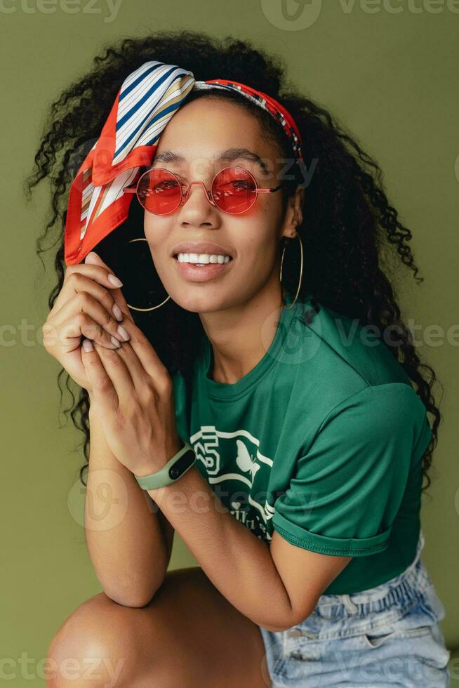 attractive black african american woman posing in stylish hipster outfit on green background photo