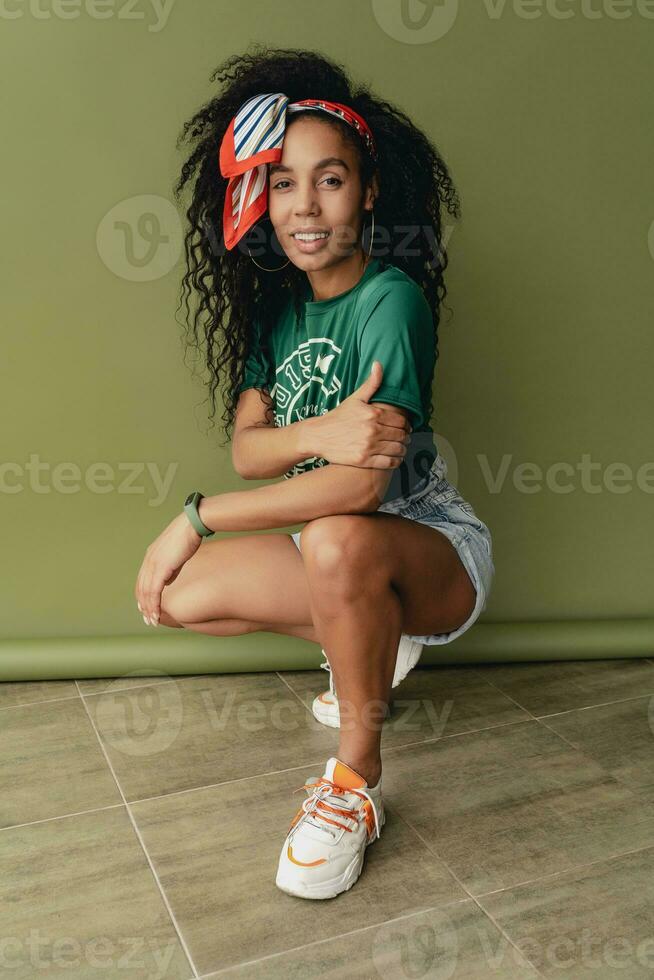 attractive black african american woman posing in stylish hipster outfit on green background photo