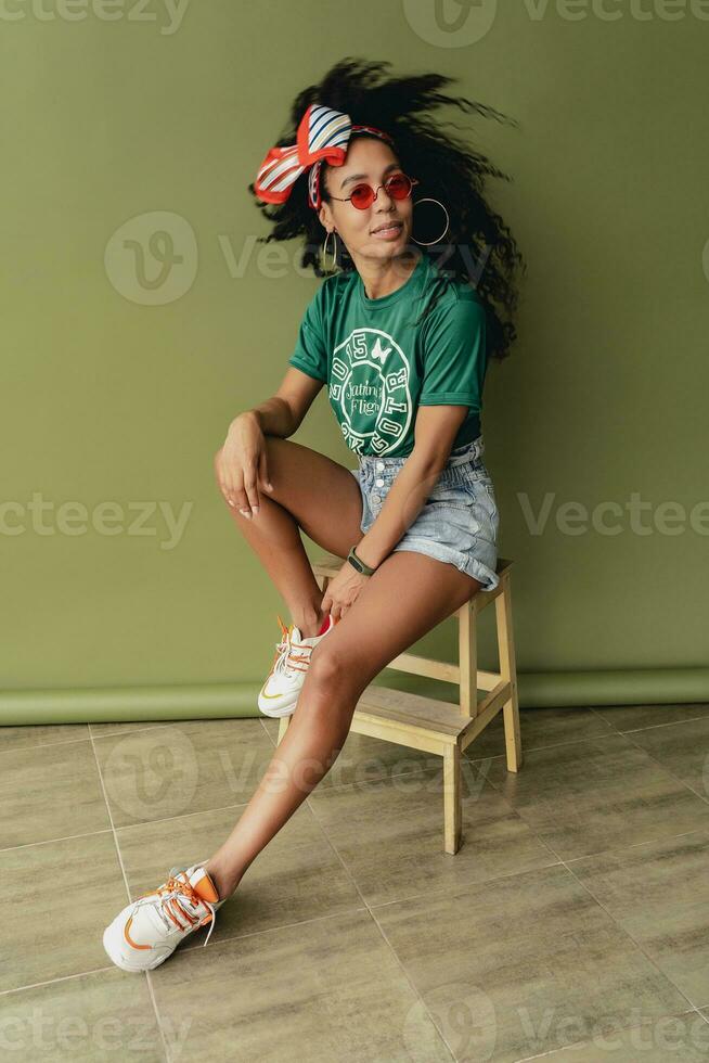 attractive black african american woman posing in stylish hipster outfit on green background photo