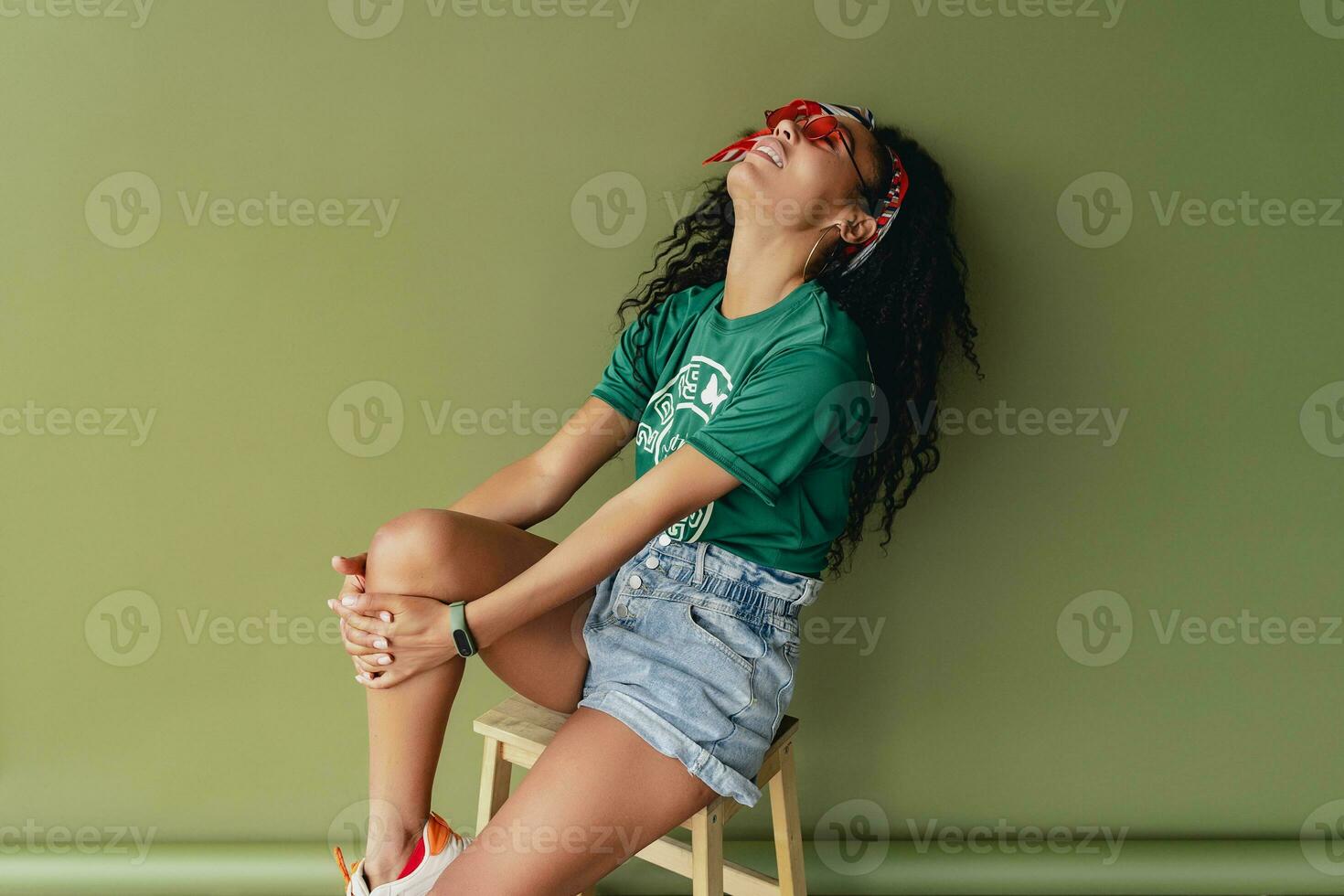 attractive black african american woman posing in stylish hipster outfit on green background photo