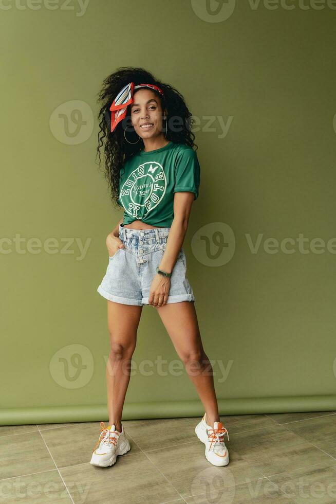 attractive black african american woman posing in stylish hipster outfit on green background photo