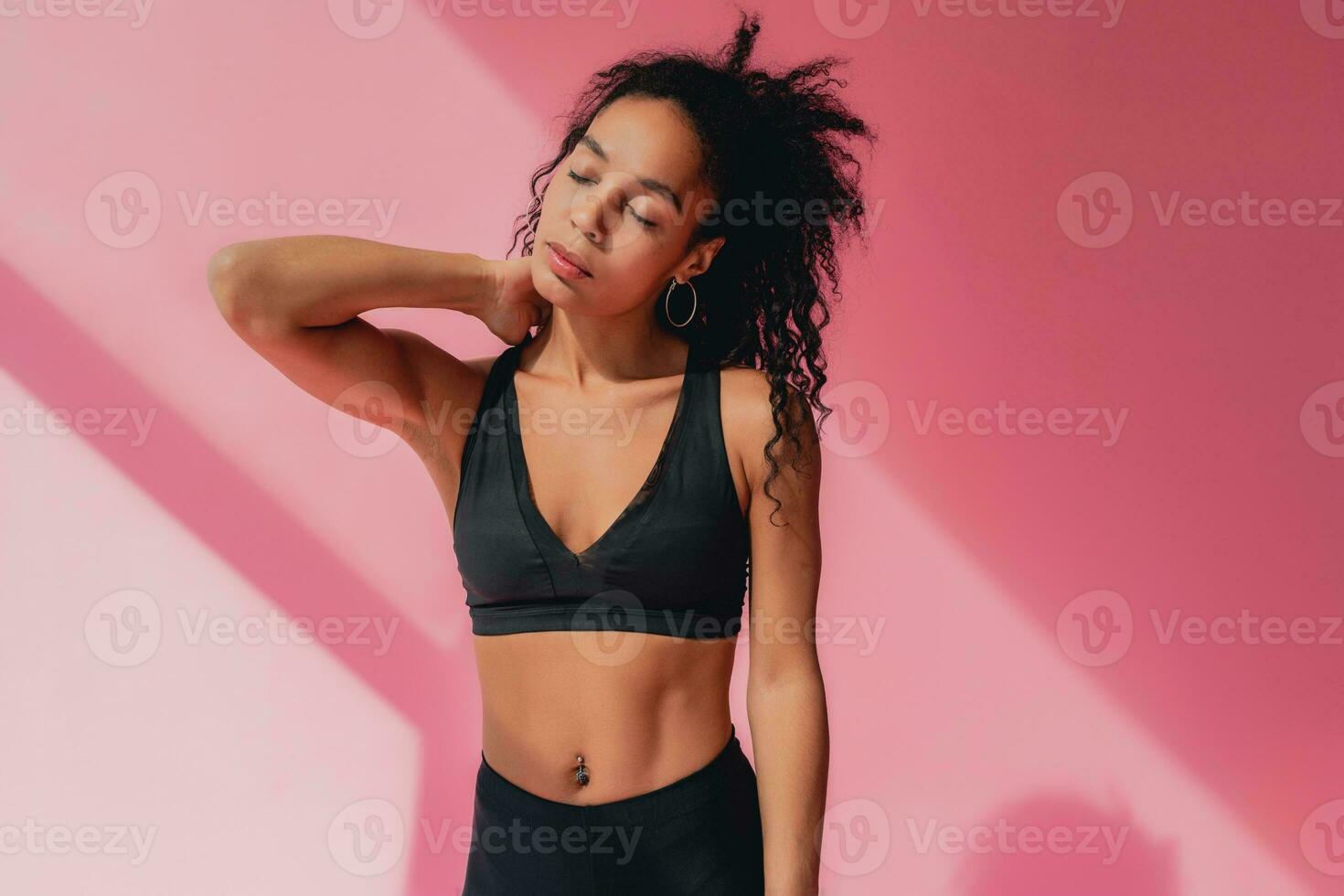 attractive black african american woman in black leggins fitness outfit on pink background photo