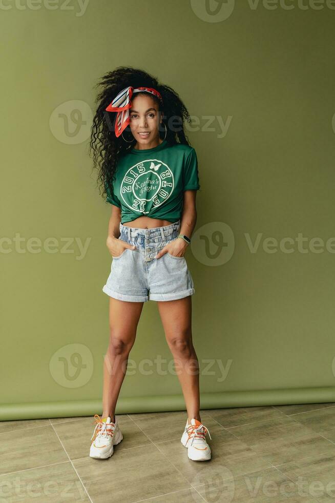 attractive black african american woman posing in stylish hipster outfit on green background photo