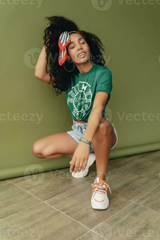 attractive black african american woman posing in stylish hipster outfit on green background photo