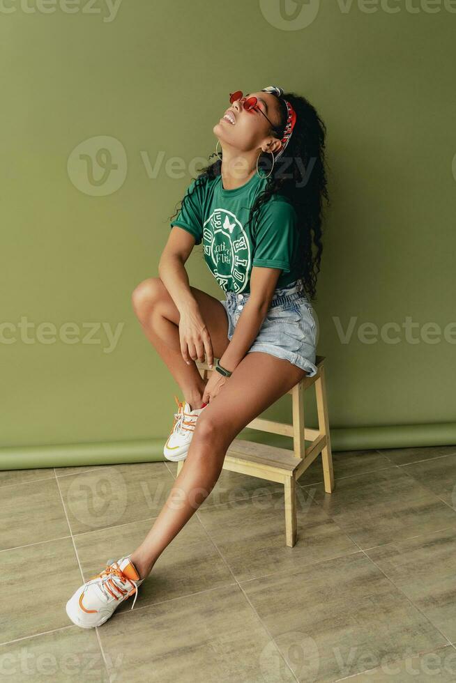 attractive black african american woman posing in stylish hipster outfit on green background photo