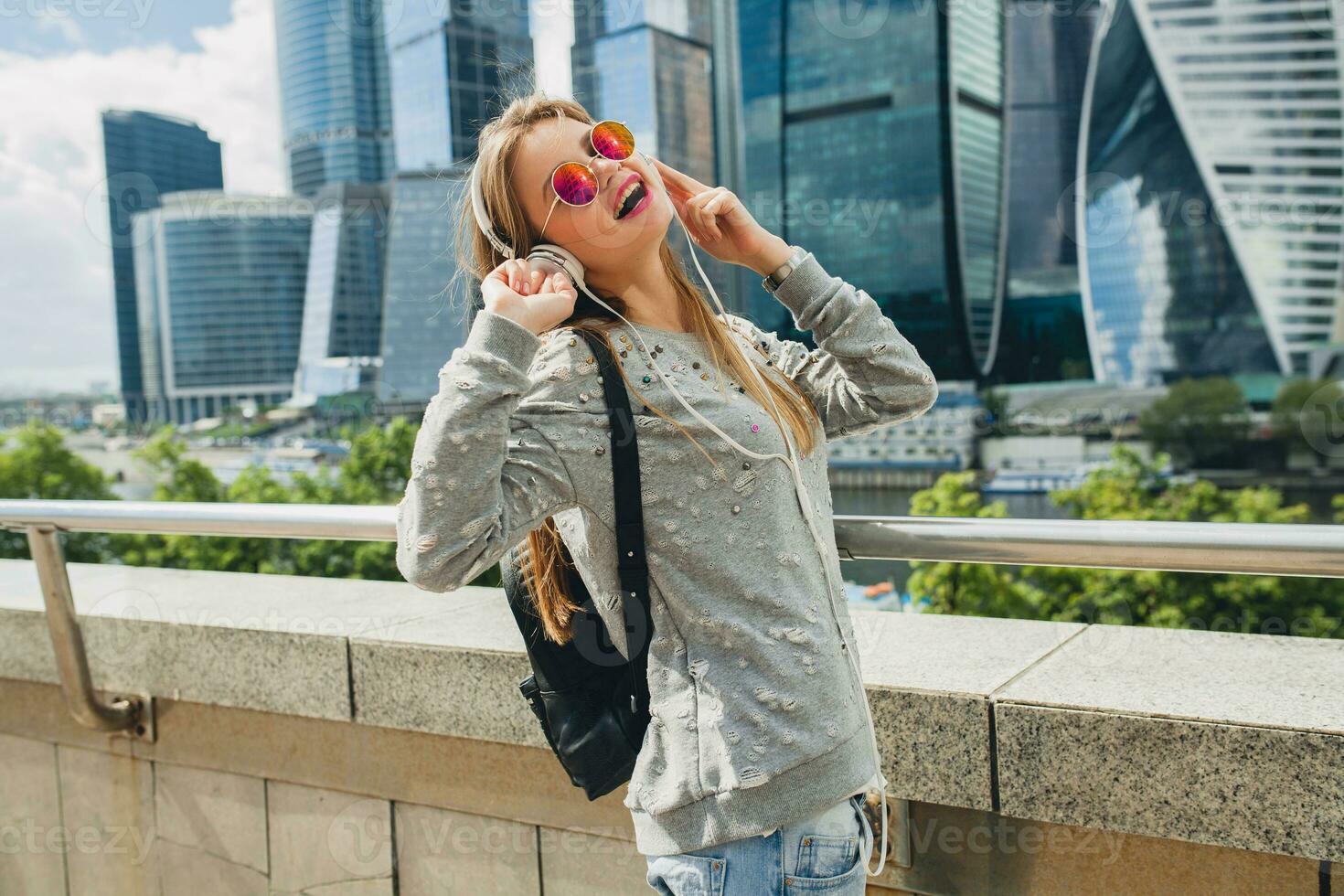 young hipster woman having fun in street listening to music on headphones photo