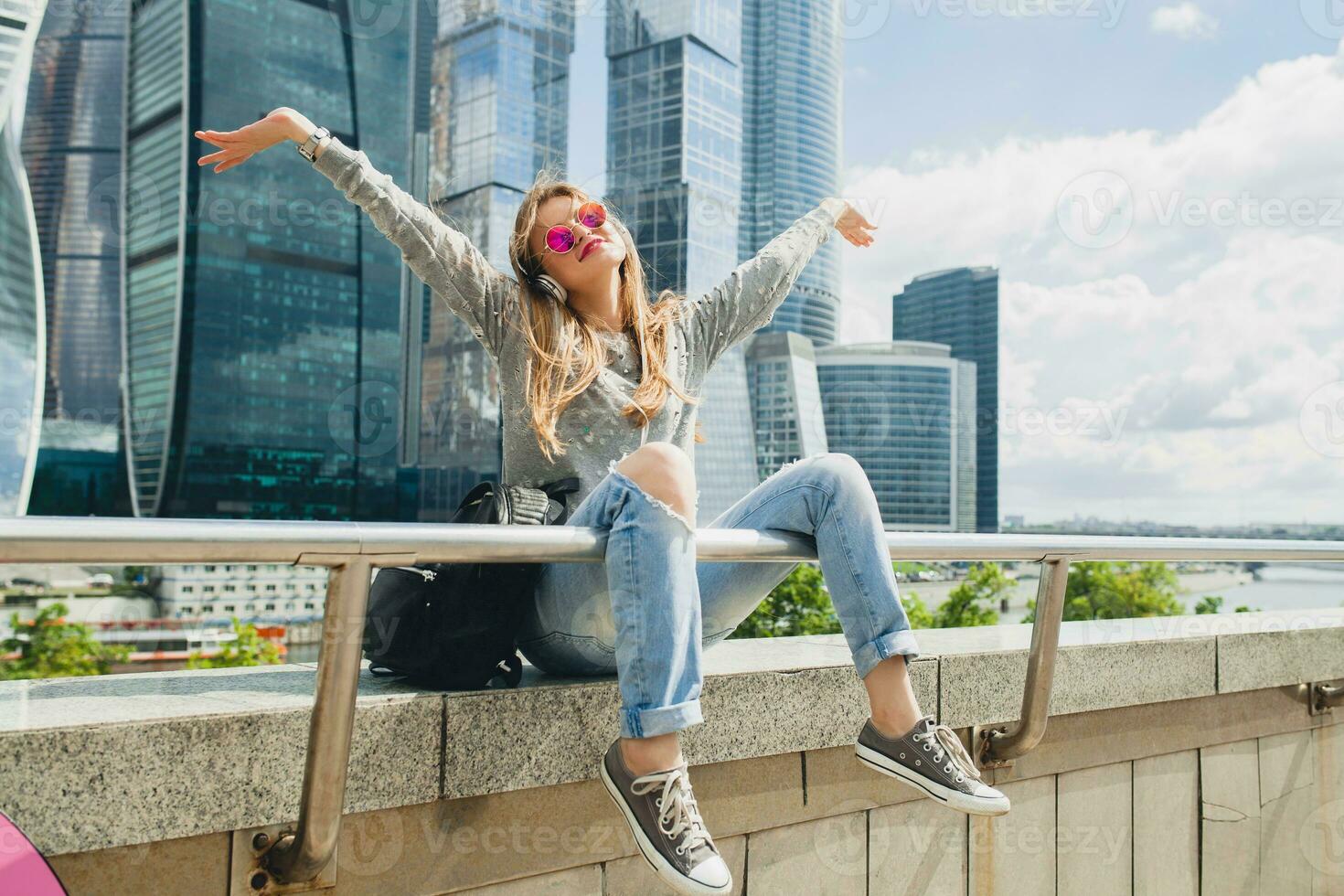 young hipster woman having fun in street listening to music on headphones photo