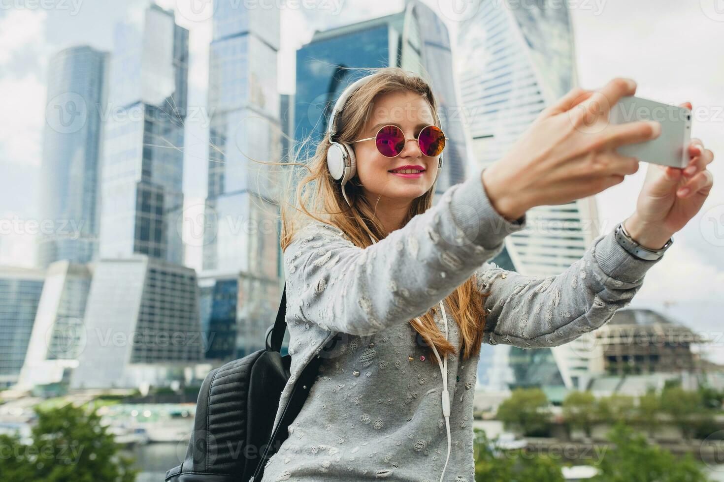 young hipster woman having fun in street listening to music on headphones photo